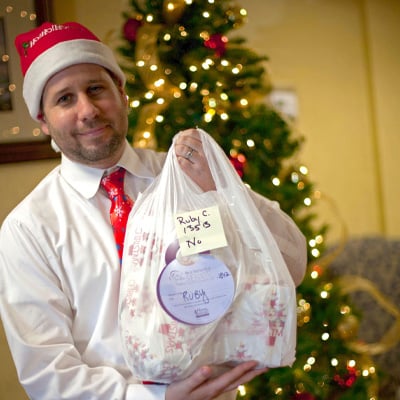 Volunteer dressed in holdiay attire holds bag of donated gifts for senior